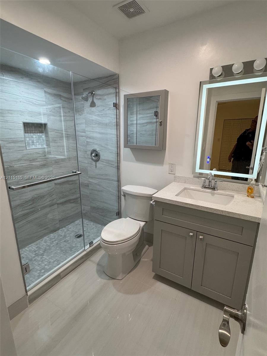 Walk-in shower featuring floor-to-ceiling tile, a built-in recessed niche, and a glass enclosure, paired with a gray vanity, solid surface countertop, and an integrated LED-lighted mirror