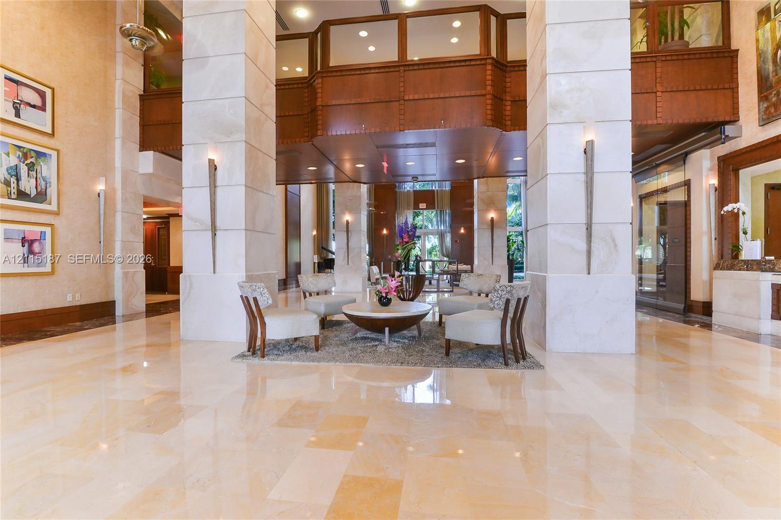 Grand lobby featuring dual-story stone-clad pillars, polished stone flooring, intricate wood-panel trim, and recessed ceiling lighting