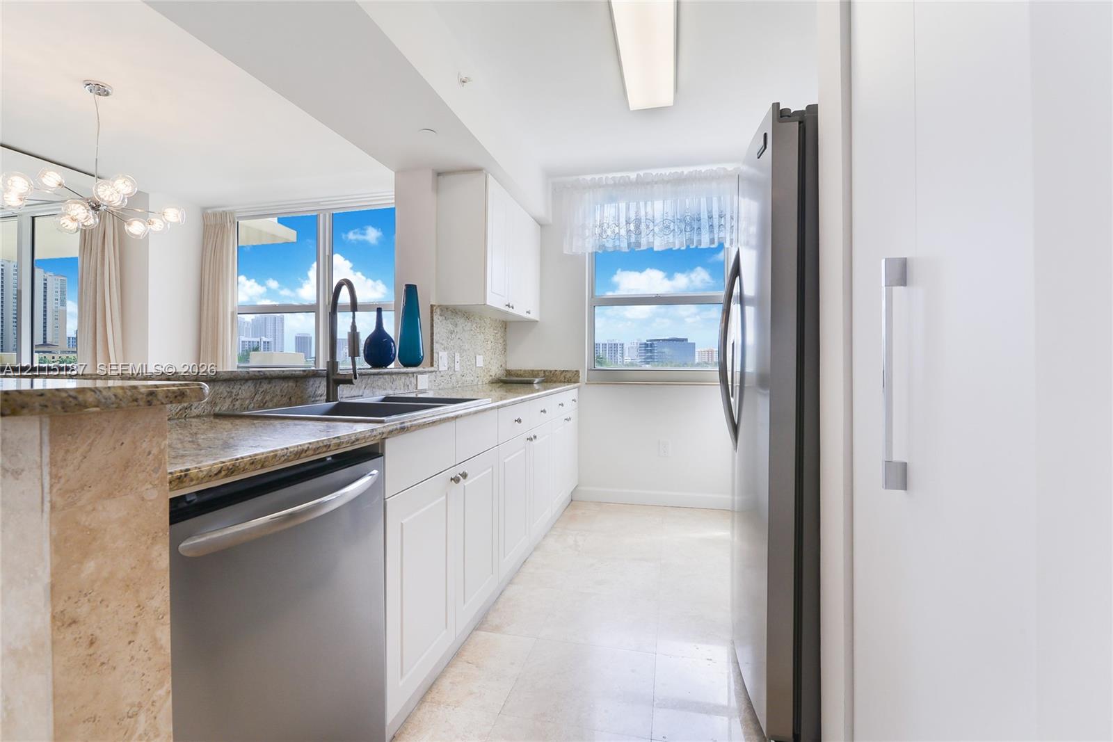 Kitchen featuring white cabinetry, stone countertops, stainless steel appliances, a double-basin undermount sink, and tile flooring Kitchen featuring white cabinetry, stone countertops, stainless steel appliances, a double-basin undermount sink, and tile flooring