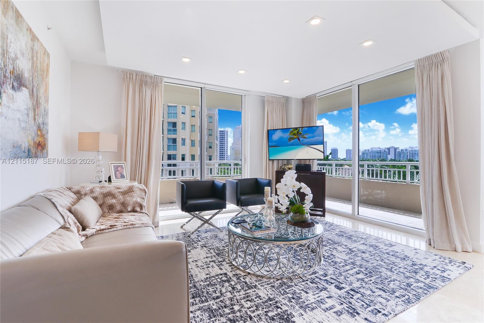 Living area featuring a tray ceiling with recessed lighting, large-format tile flooring, and expansive floor-to-ceiling glass sliding doors providing access to a covered balcony with a glass railing Living area featuring a tray ceiling with recessed lighting, large-format tile flooring, and expansive floor-to-ceiling glass sliding doors providing access to a covered balcony with a glass railing