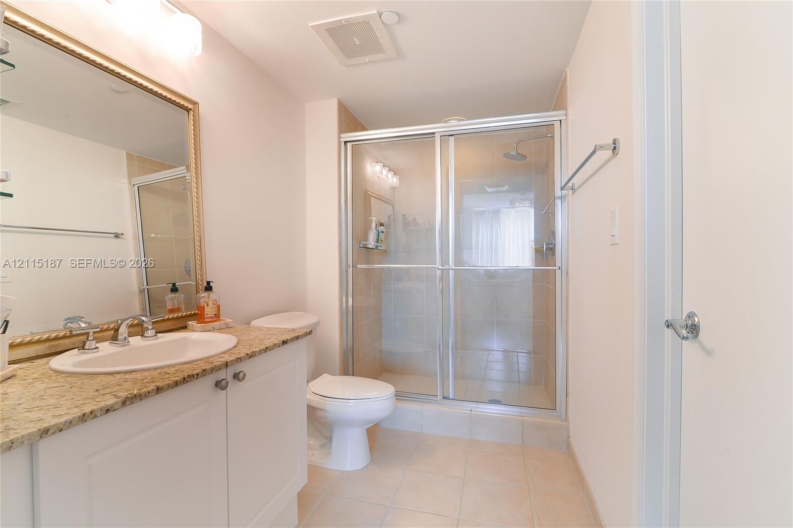 Bathroom featuring a vanity with a stone-finish countertop, undermount sink, framed wall mirror, and a walk-in glass-enclosed shower Bathroom featuring a vanity with a stone-finish countertop, undermount sink, framed wall mirror, and a walk-in glass-enclosed shower