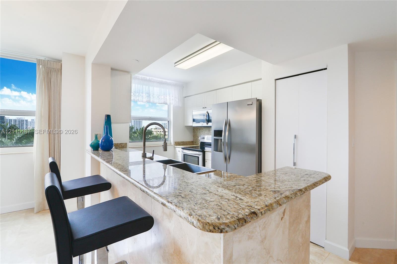 Kitchen featuring a peninsula with a stone countertop, stainless steel refrigerator, built-in microwave, drop-in dual basin sink with gooseneck faucet, and flat-panel cabinetry Kitchen featuring a peninsula with a stone countertop, stainless steel refrigerator, built-in microwave, drop-in dual basin sink with gooseneck faucet, and flat-panel cabinetry