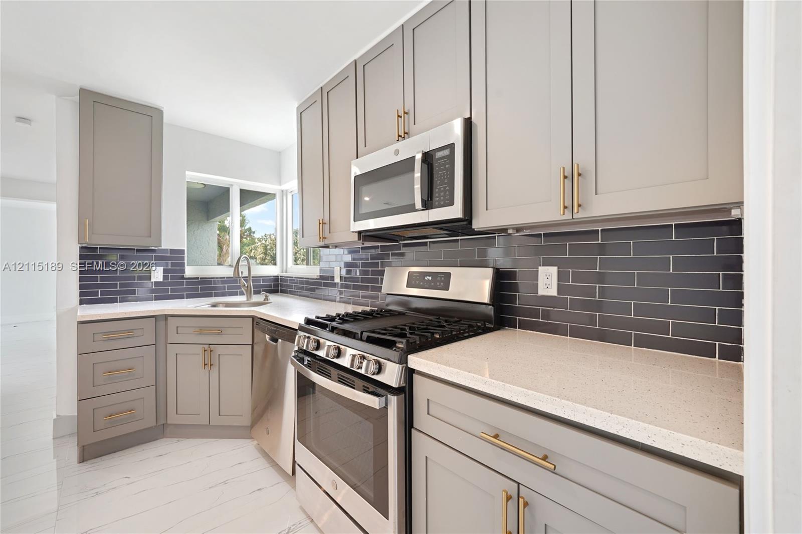 Kitchen featuring shaker-style cabinetry with gold-tone hardware, polished solid surface countertops, dark subway tile backsplash, stainless steel appliances, and white wood-finish flooring