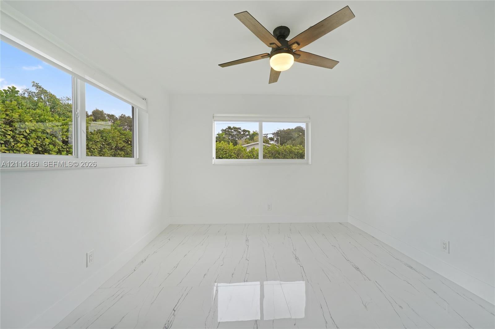 Room featuring white stone-finish flooring with grey veining, two horizontal sliding windows, and a ceiling-mounted fan with integrated light fixture