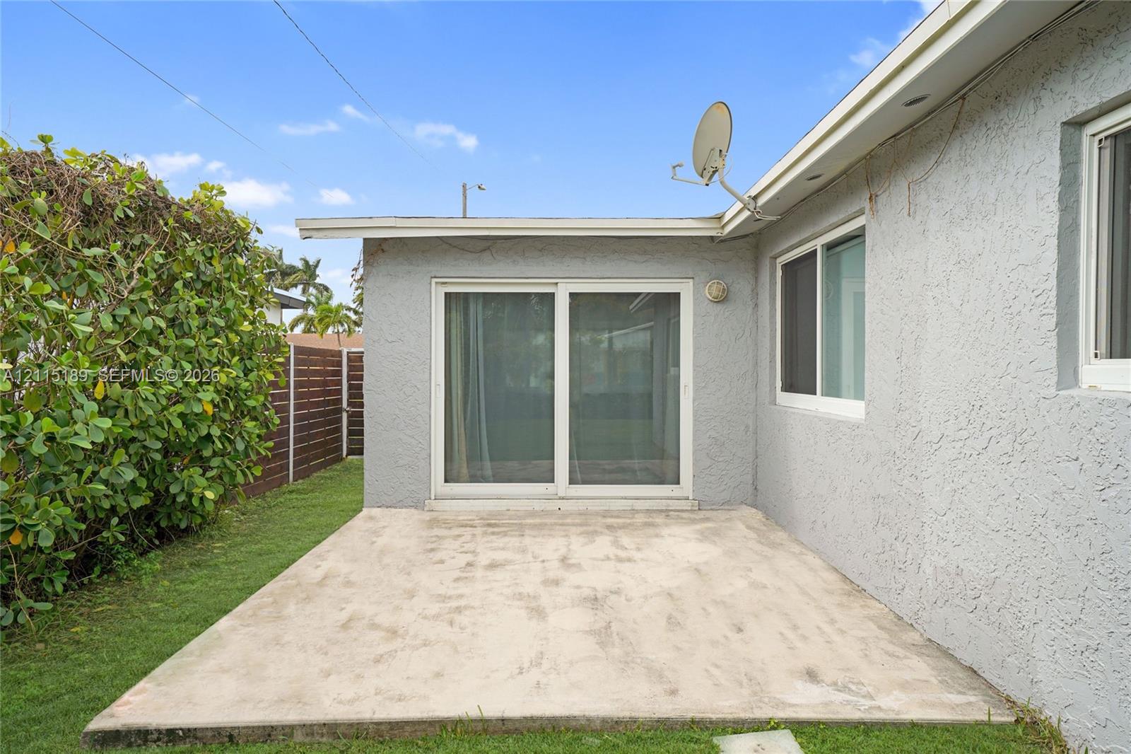 Concrete patio featuring sliding glass doors, stucco exterior walls, and privacy fencing