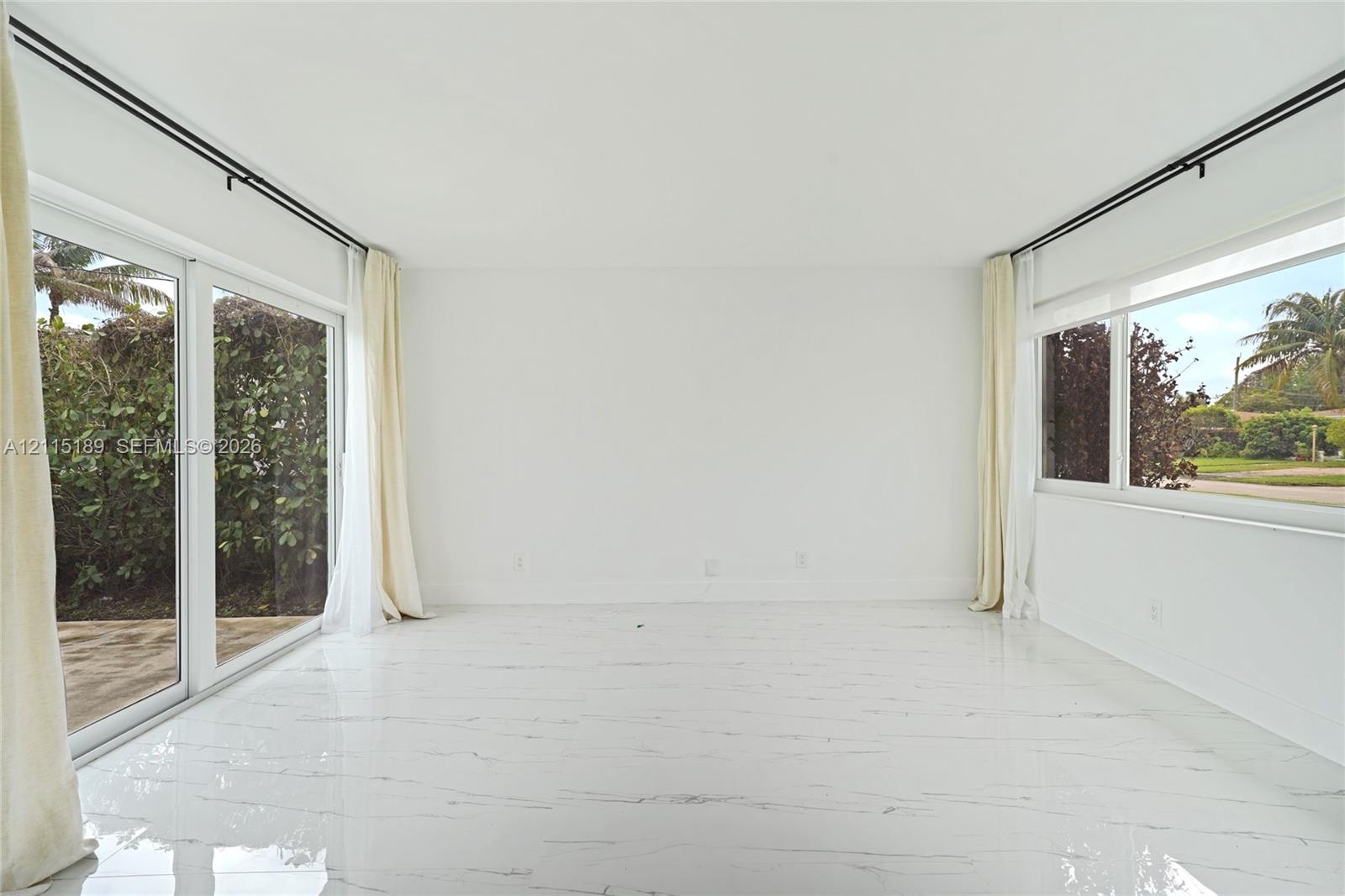 Bright room featuring white tile flooring with grey veining, expansive sliding glass doors, and large windows with black curtain hardware Bright room featuring white tile flooring with grey veining, expansive sliding glass doors, and large windows with black curtain hardware