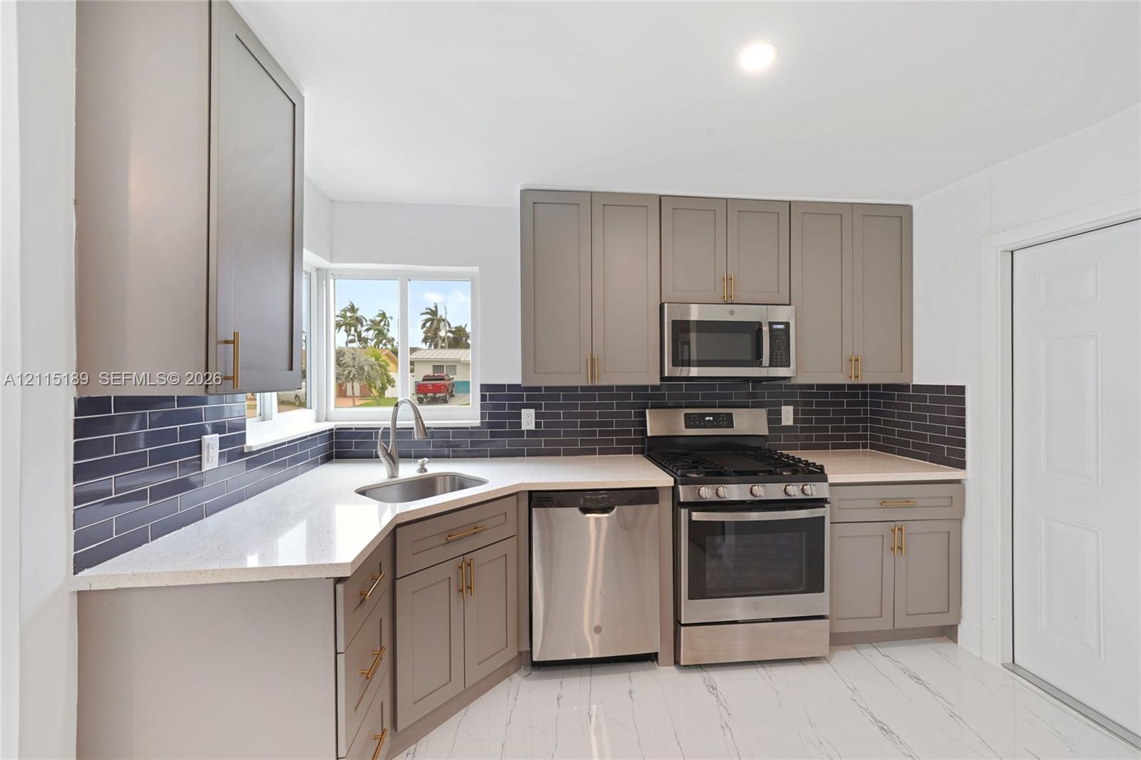 Kitchen featuring shaker-style cabinetry, dark tile backsplash, stainless steel appliances, light-toned countertops, and an undermount sink