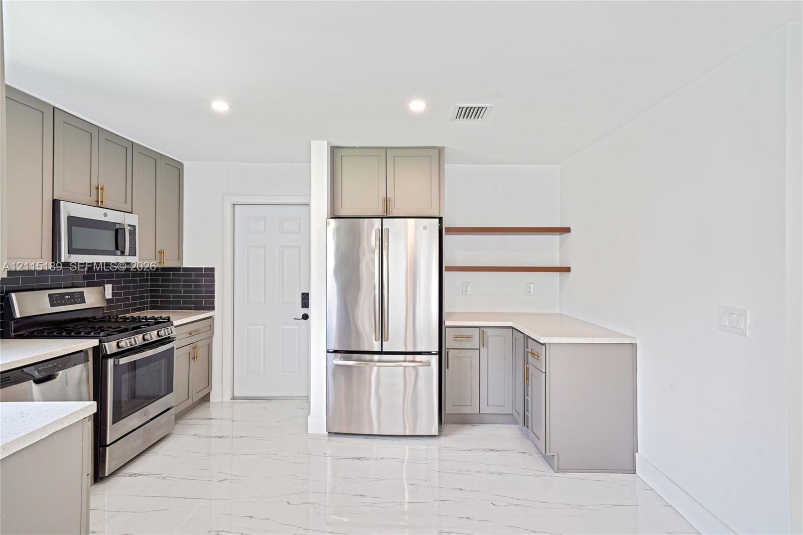 Kitchen featuring shaker-style cabinetry, stainless steel appliances, quartz countertops, dark subway tile backsplash, and polished stone-finish flooring