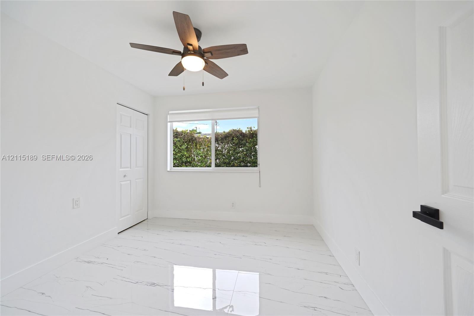 Interior room featuring white-veined tile flooring, a multi-blade ceiling fan with integrated lighting, a sliding window with a roller shade, and doors with matte black hardware