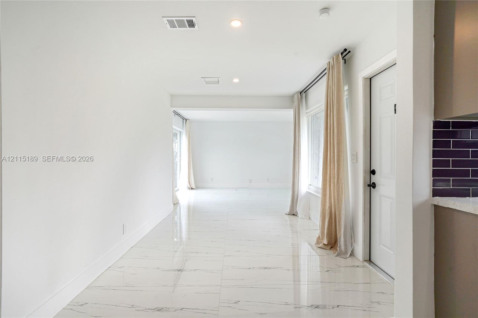 Open-concept living space featuring high-gloss, light-toned stone-finish tile flooring, recessed lighting, and a neutral color palette Open-concept living space featuring high-gloss, light-toned stone-finish tile flooring, recessed lighting, and a neutral color palette