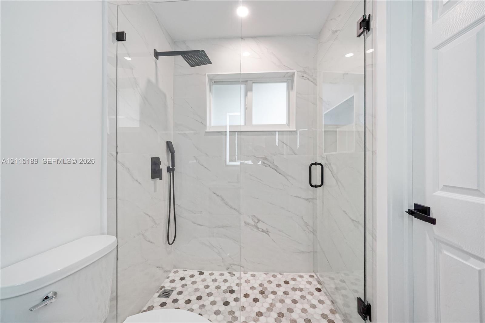 Walk-in shower featuring floor-to-ceiling stone-finish tile walls, hexagonal mosaic floor tile, frameless glass enclosure, and matte black plumbing fixtures