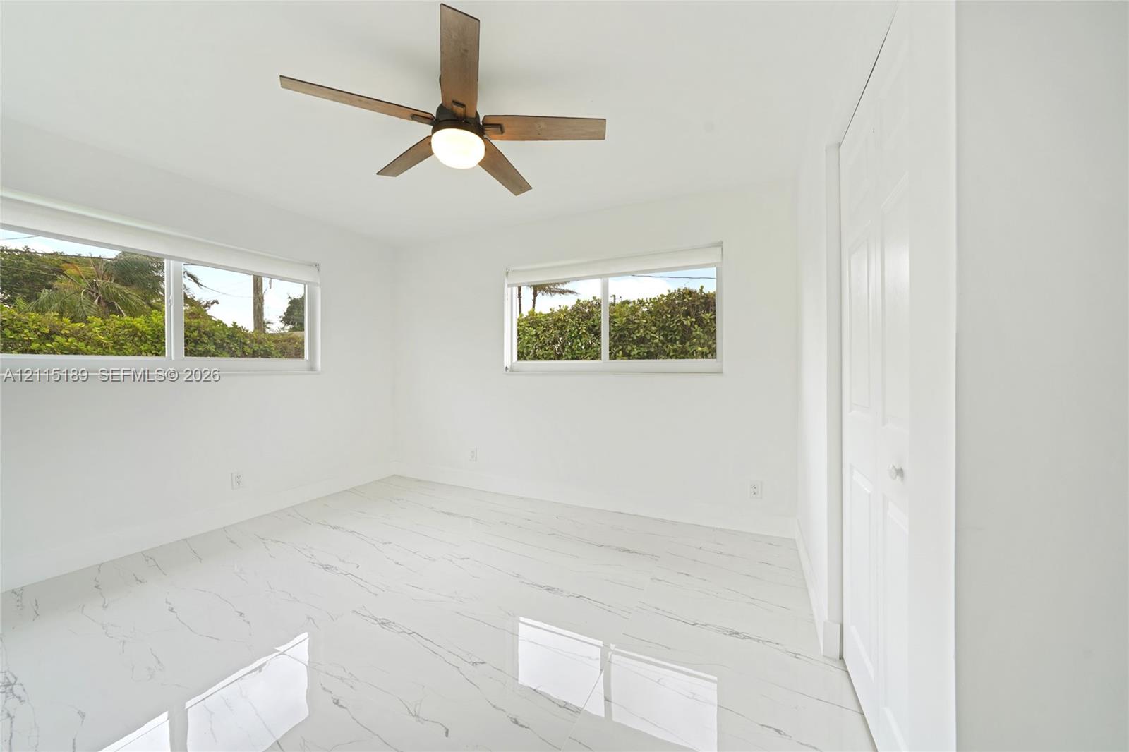 Interior space featuring large-format tile flooring with veining detail, multi-pane sliding windows, and a ceiling fan with integrated lighting