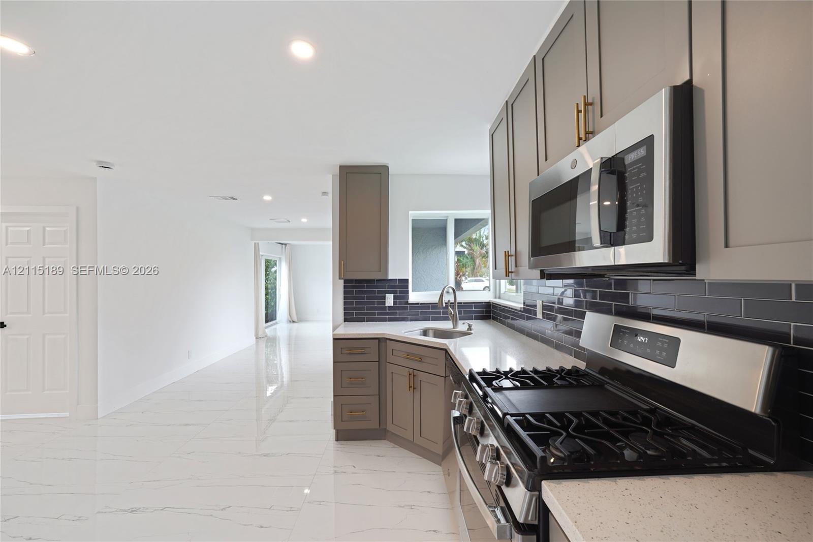 Kitchen featuring grey Shaker-style cabinetry, quartz countertops, a dark subway tile backsplash, stainless steel appliances, and large-format tile flooring