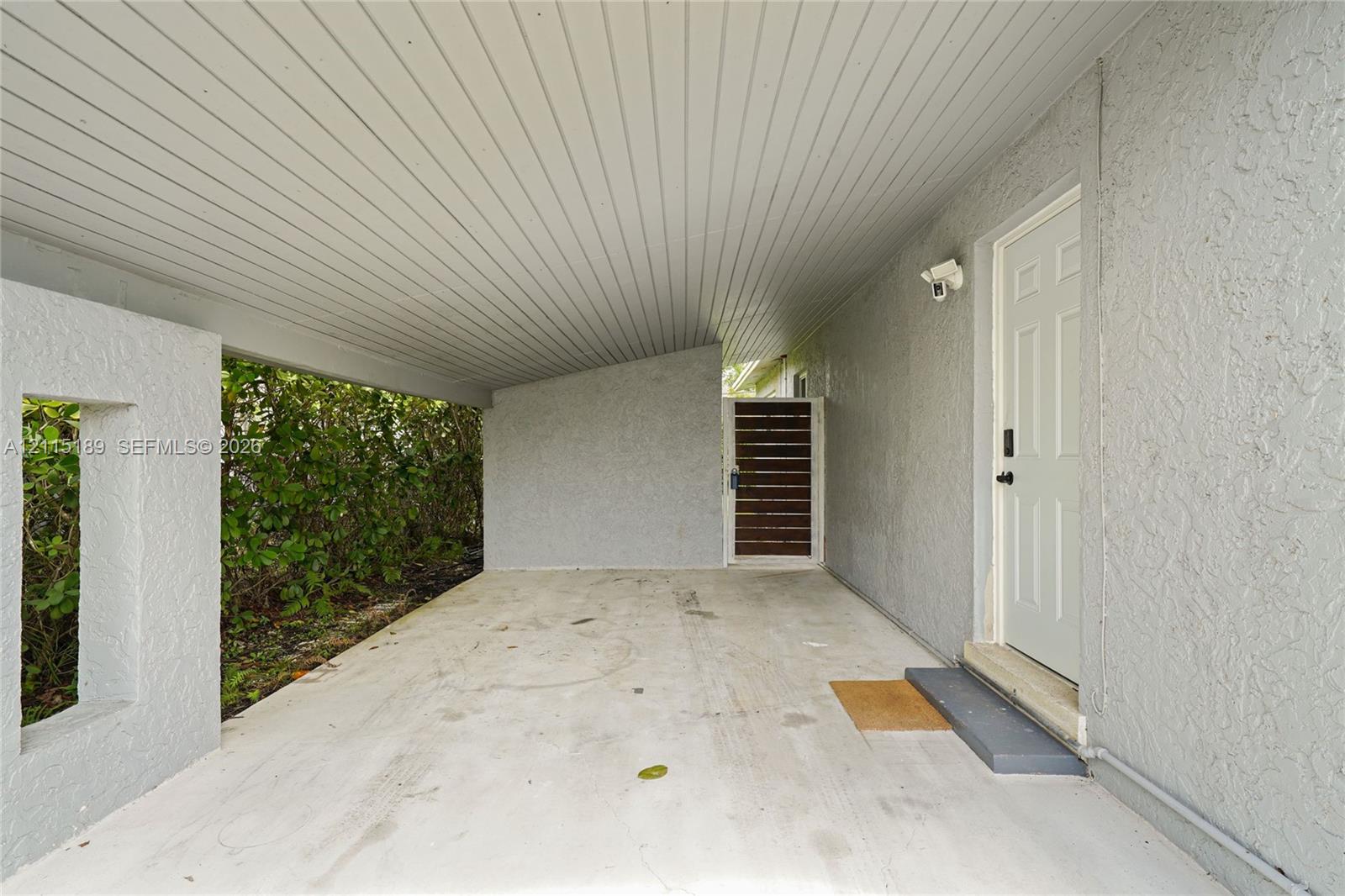 Covered carport featuring a concrete floor, textured stucco exterior walls, a beadboard-style ceiling, and a wooden slat privacy gate
