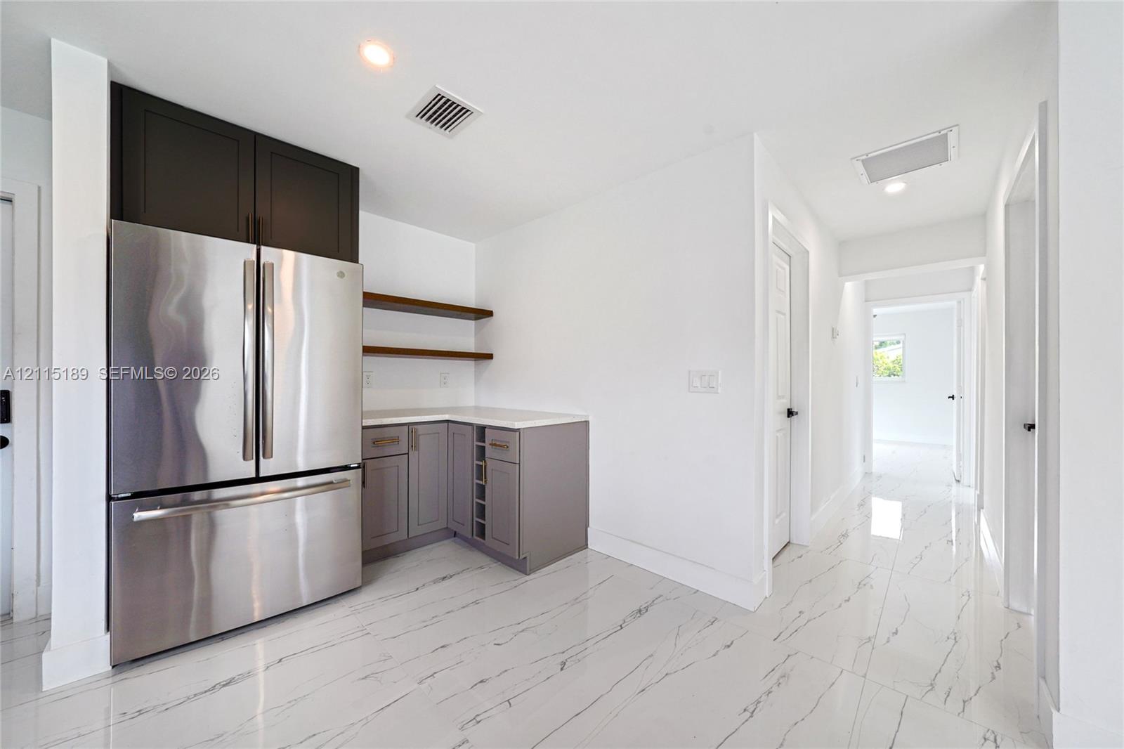 Stainless steel French-door refrigerator, custom cabinetry with integrated wine storage, quartz countertops, floating wall shelving, and polished stone-finish flooring