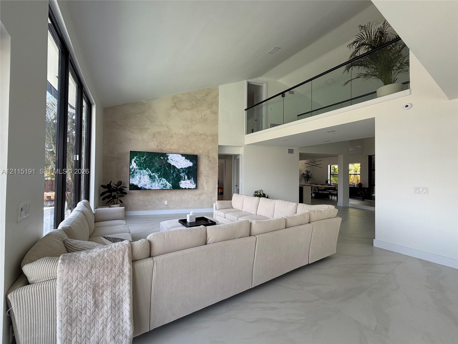 Double-height ceiling, textured accent wall, floor-to-ceiling windows, porcelain tile flooring, and glass-paneled interior railing Double-height ceiling, textured accent wall, floor-to-ceiling windows, porcelain tile flooring, and glass-paneled interior railing