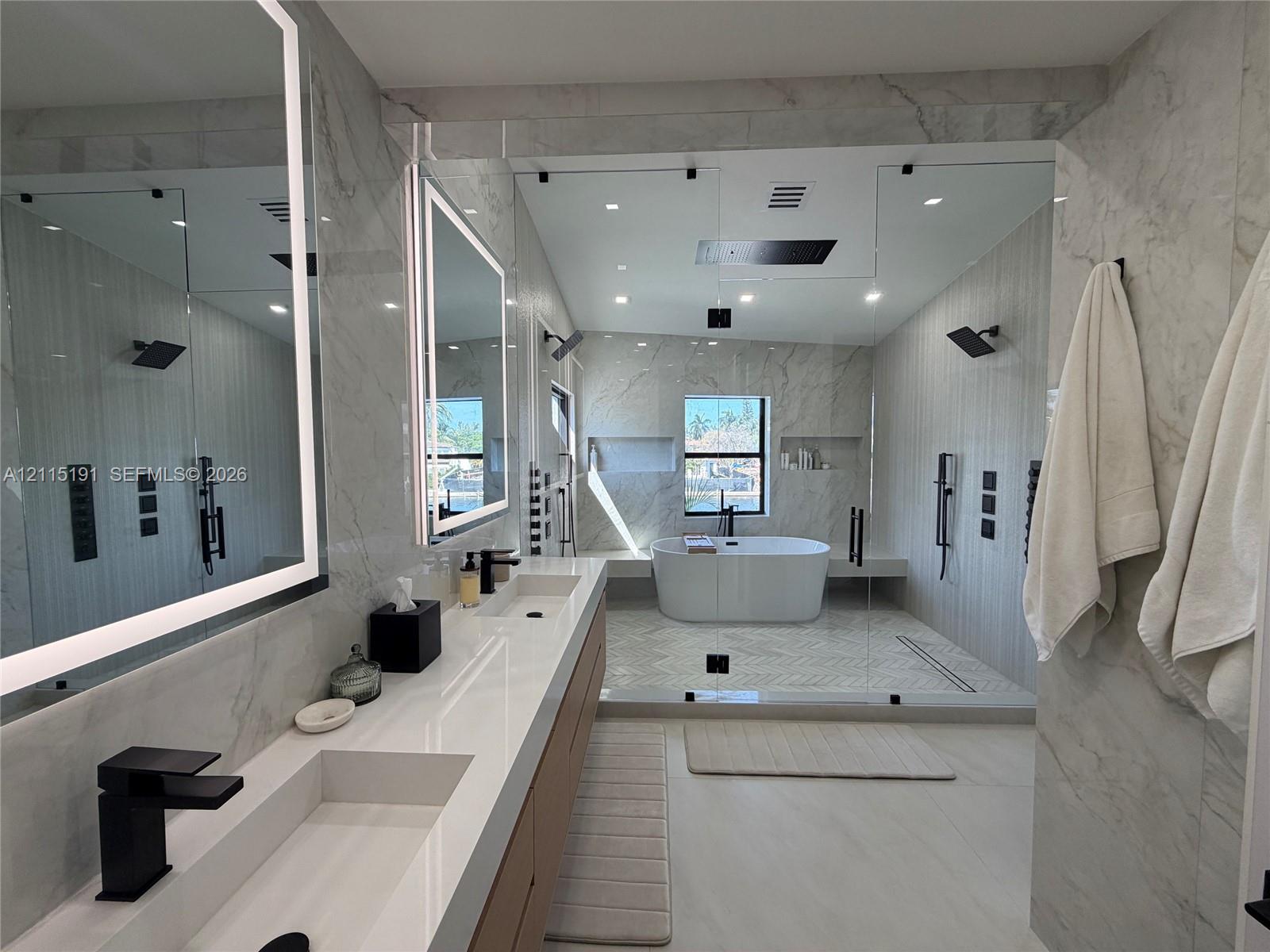 Dual-vanity cabinet with white composite countertops, integrated rectangular sinks, and matte black fixtures, paired with backlit vanity mirrors Dual-vanity cabinet with white composite countertops, integrated rectangular sinks, and matte black fixtures, paired with backlit vanity mirrors