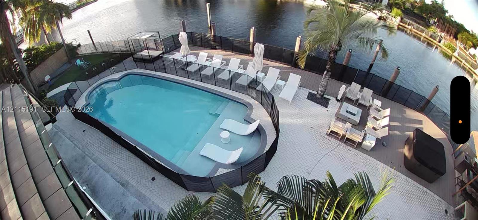 Waterfront pool area featuring a built-in sun shelf, perimeter safety fencing, paved patio, and dockage Waterfront pool area featuring a built-in sun shelf, perimeter safety fencing, paved patio, and dockage