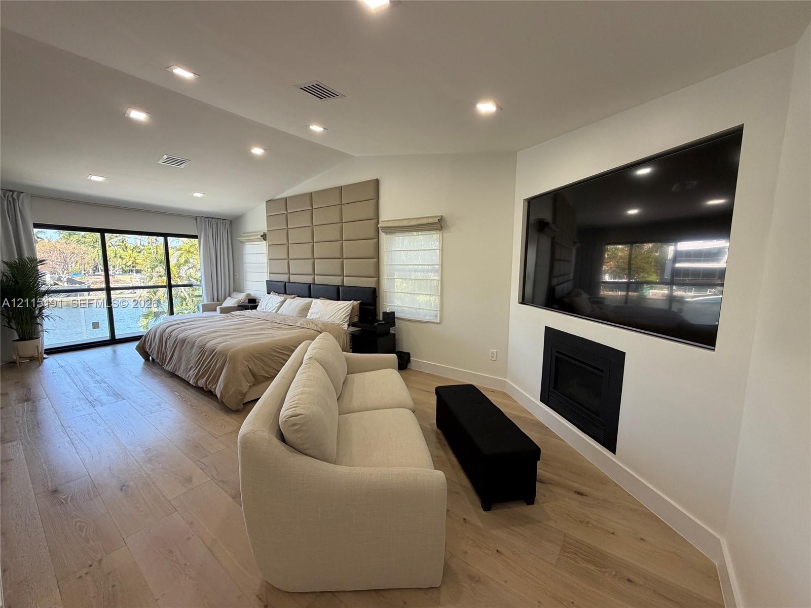 Vaulted ceilings with recessed lighting, wood-finish flooring, custom upholstered wall paneling, built-in fireplace, and expansive black-framed sliding glass doors Vaulted ceilings with recessed lighting, wood-finish flooring, custom upholstered wall paneling, built-in fireplace, and expansive black-framed sliding glass doors