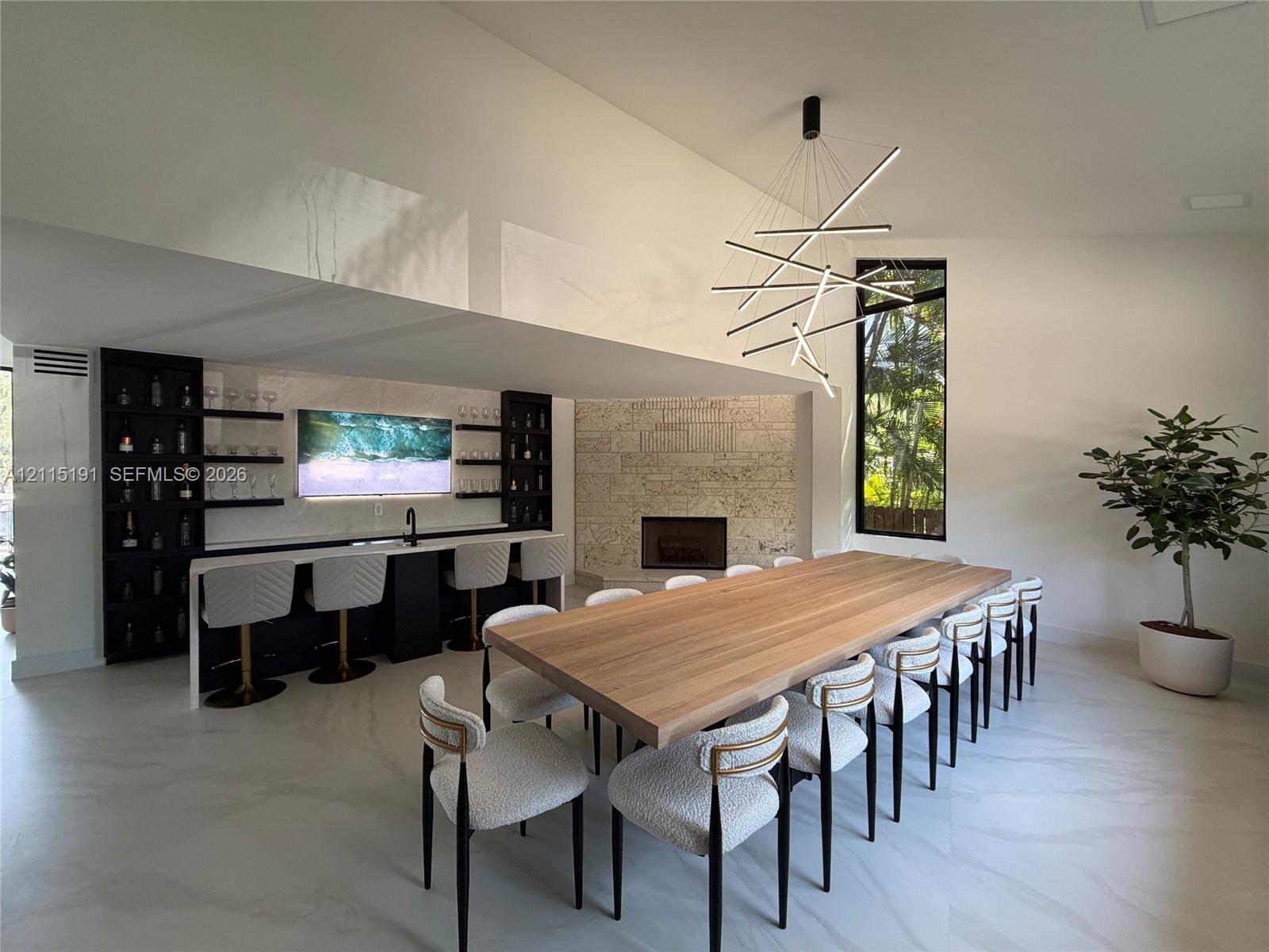 Built-in wet bar with dark cabinetry, floating shelving, and integrated sink, stone-faced fireplace, modern geometric chandelier, and large-format flooring Built-in wet bar with dark cabinetry, floating shelving, and integrated sink, stone-faced fireplace, modern geometric chandelier, and large-format flooring