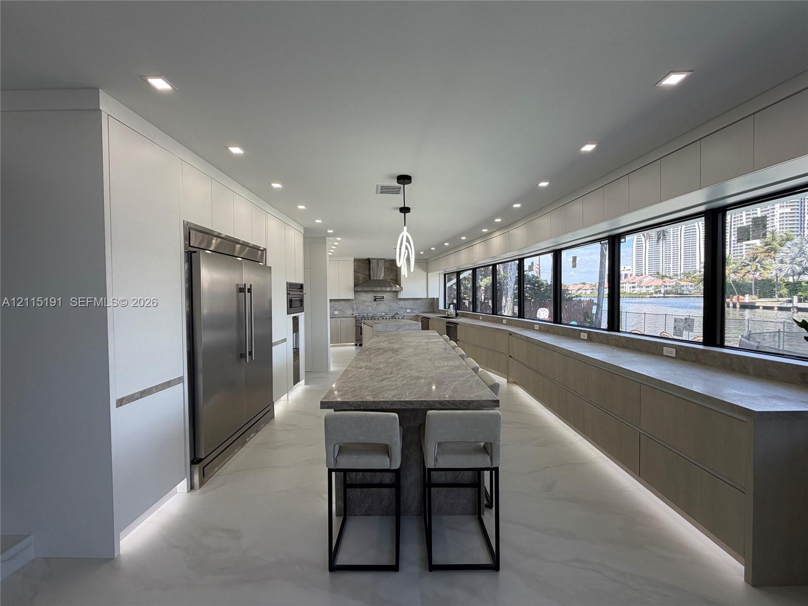 Kitchen featuring matte-finish cabinetry, a large stone-topped central island, integrated stainless steel appliances, recessed lighting, and expansive windows Kitchen featuring matte-finish cabinetry, a large stone-topped central island, integrated stainless steel appliances, recessed lighting, and expansive windows