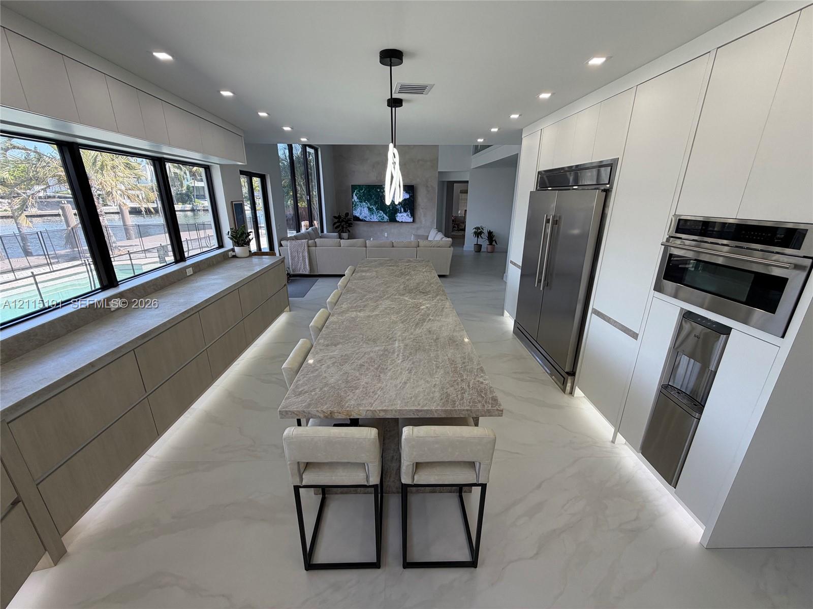 Contemporary kitchen featuring floor-to-ceiling cabinetry, a central stone-topped island with integrated base lighting, stainless steel appliances, and large-format tile flooring Contemporary kitchen featuring floor-to-ceiling cabinetry, a central stone-topped island with integrated base lighting, stainless steel appliances, and large-format tile flooring