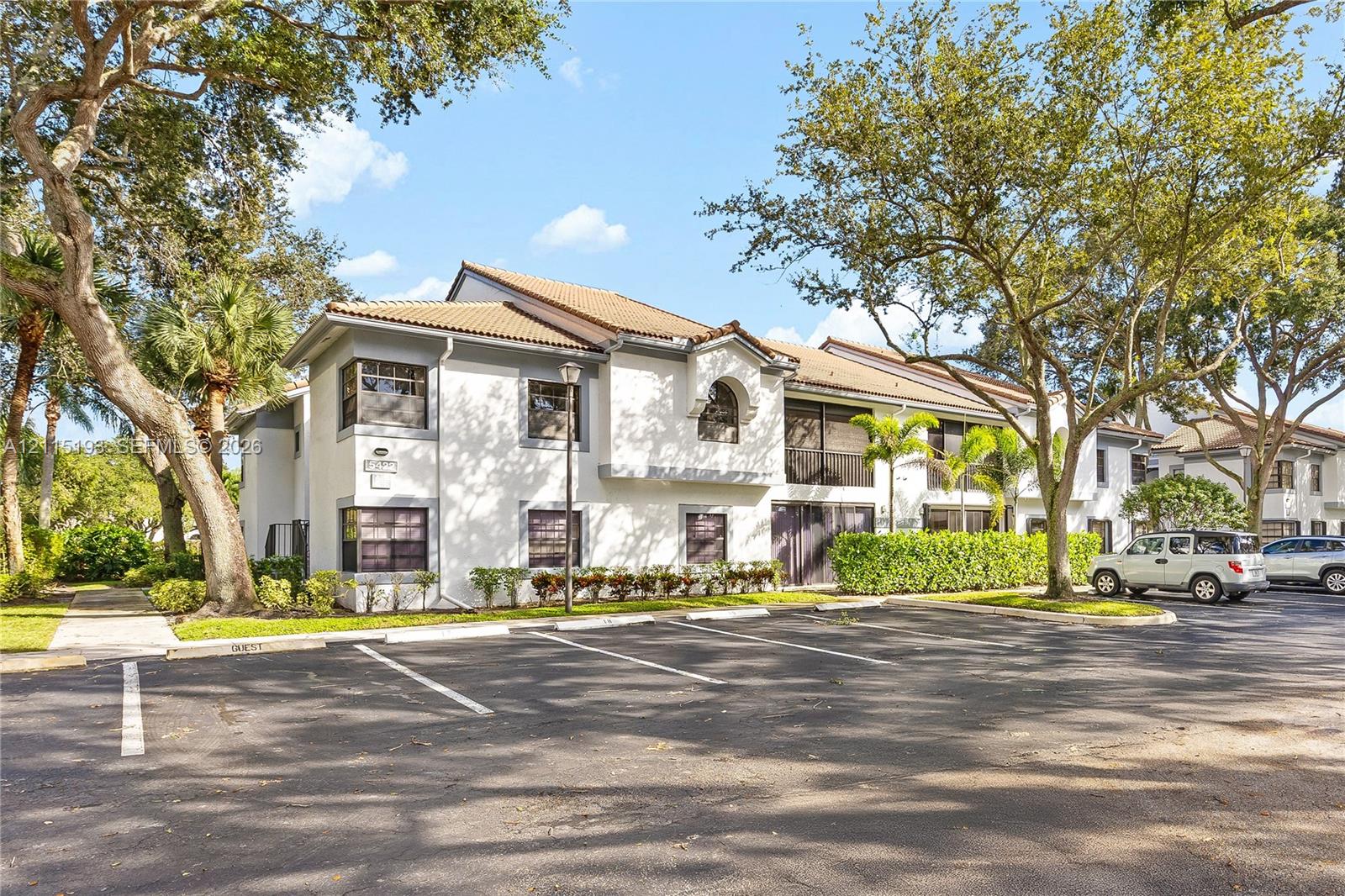 Stucco exterior with a tiled roof, mature landscaping, and paved parking area Stucco exterior with a tiled roof, mature landscaping, and paved parking area