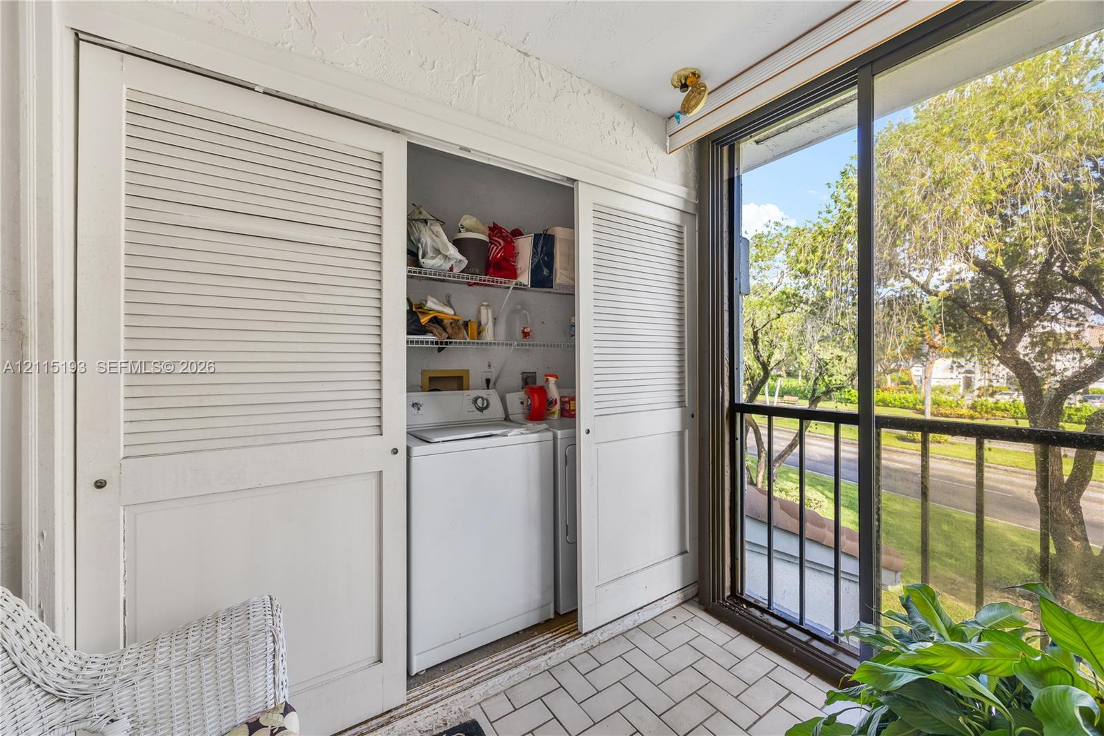 Enclosed balcony featuring a tile floor, white louvered sliding closet doors, built-in wire shelving, and floor-to-ceiling glass sliding doors with metal frame
