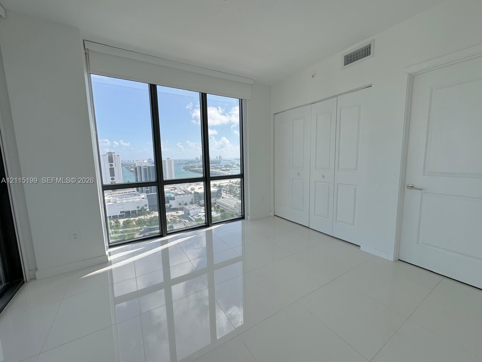 Floor-to-ceiling windows, polished tile flooring, white-panel bifold closet doors, and solid-core door with metallic hardware