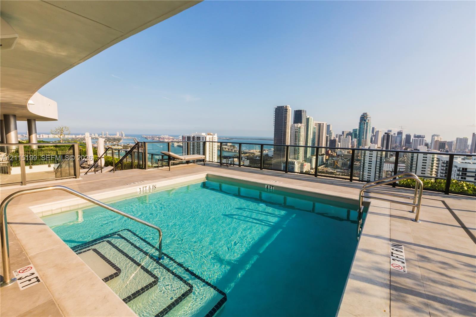 Rooftop swimming pool featuring stone tile decking, stainless steel handrails, a glass panel perimeter railing, and a cityscape backdrop