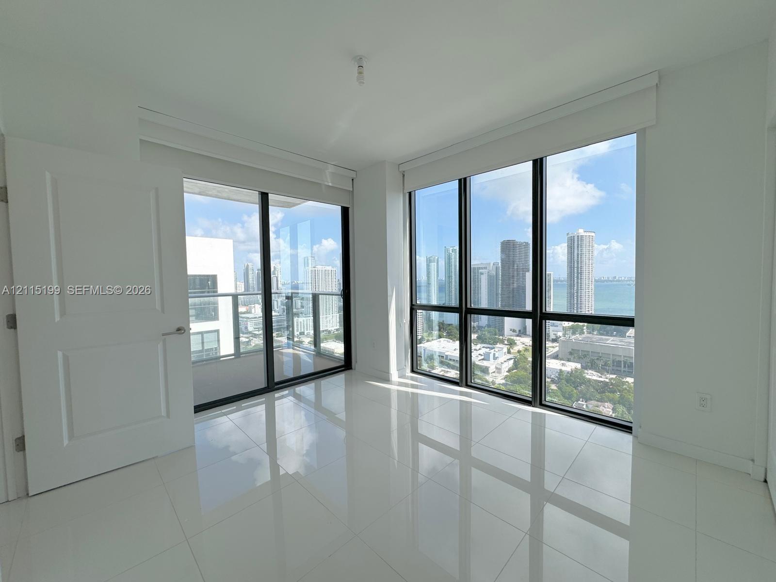 Floor-to-ceiling windows with black frames, polished tile flooring, glass-railed balcony, and skyline scenery