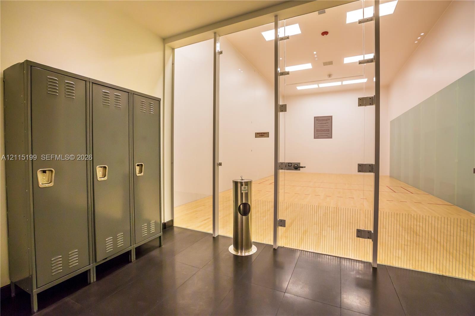 Recreational court featuring wood flooring, high-clearance ceiling with recessed lighting, glass-paneled partition, and industrial-finish metal lockers