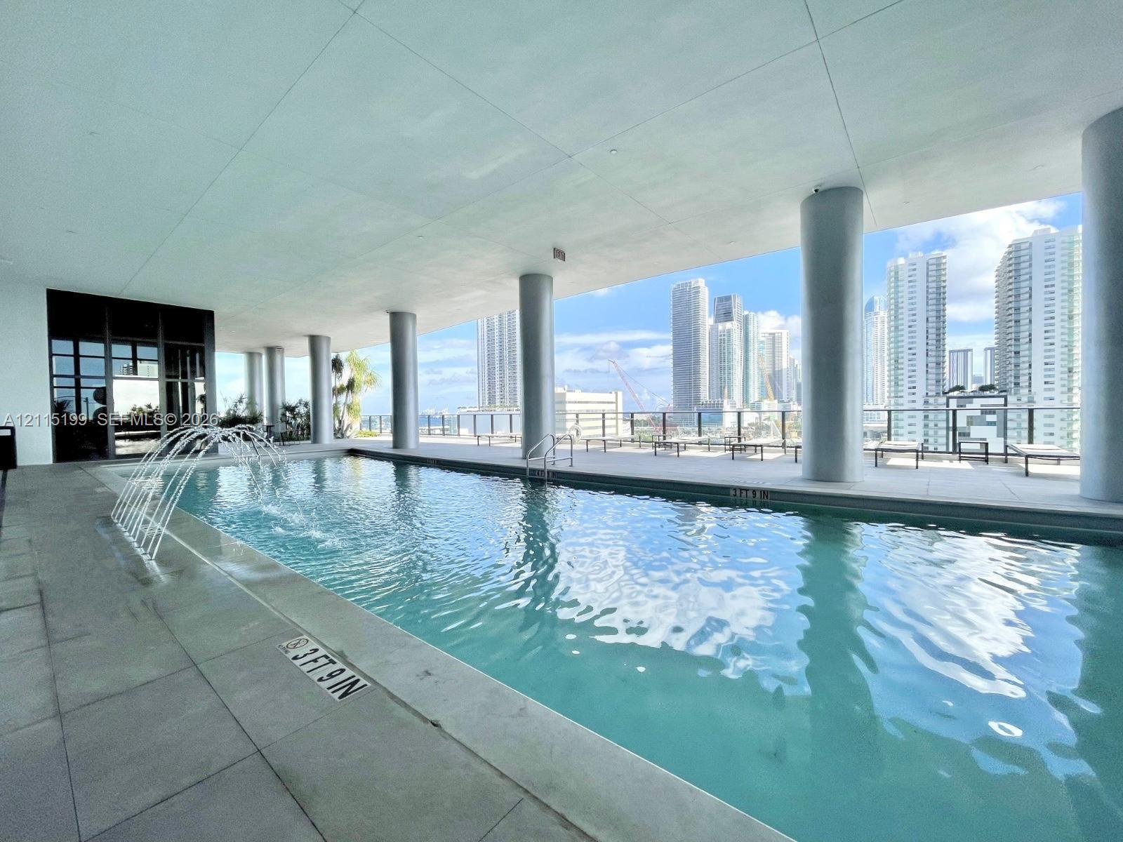 Covered outdoor pool featuring a water fountain element, large-format tile decking, and structural support columns
