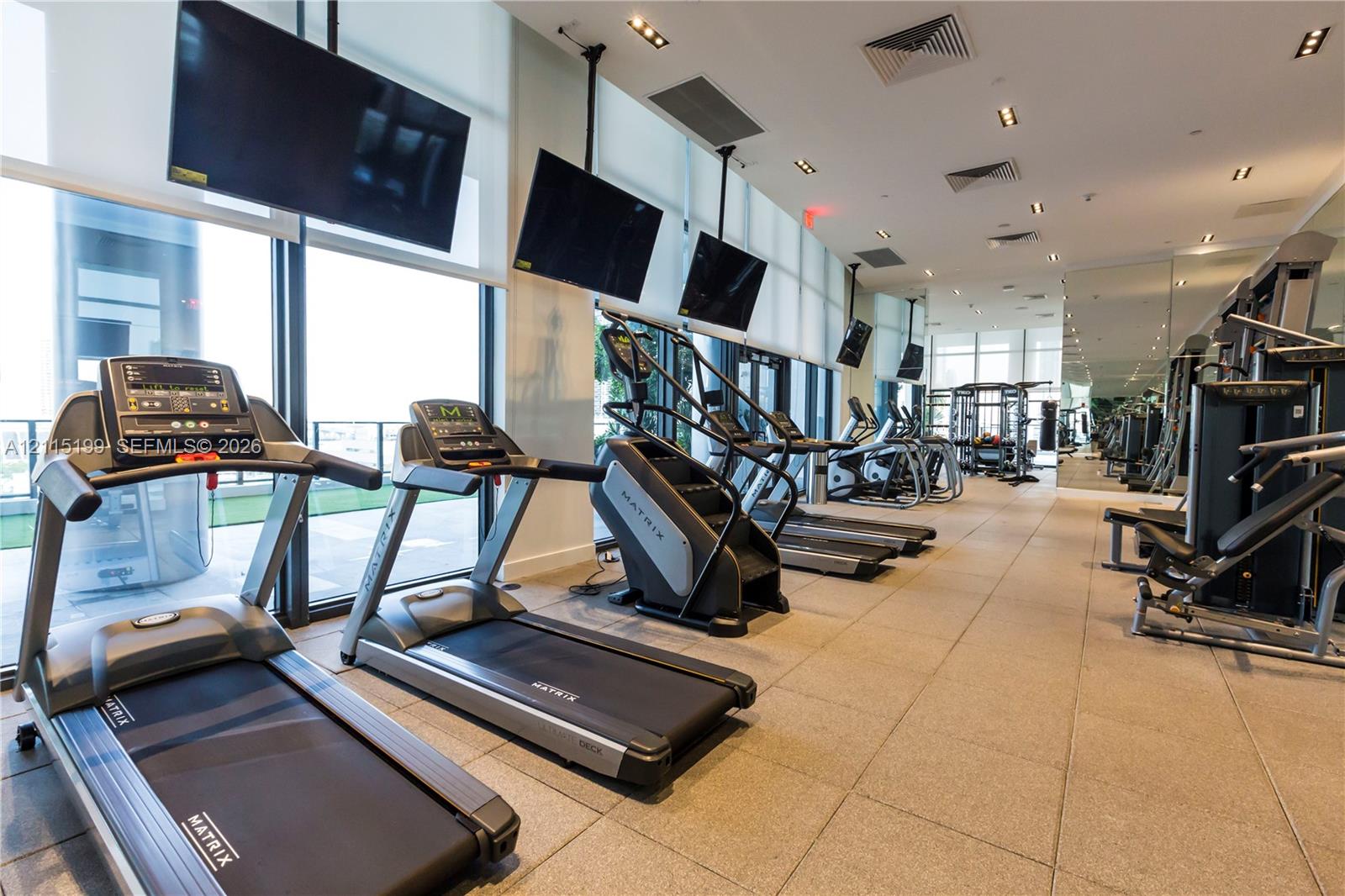 Fitness center featuring floor-to-ceiling windows, tile flooring, recessed ceiling lighting, and wall-mounted televisions