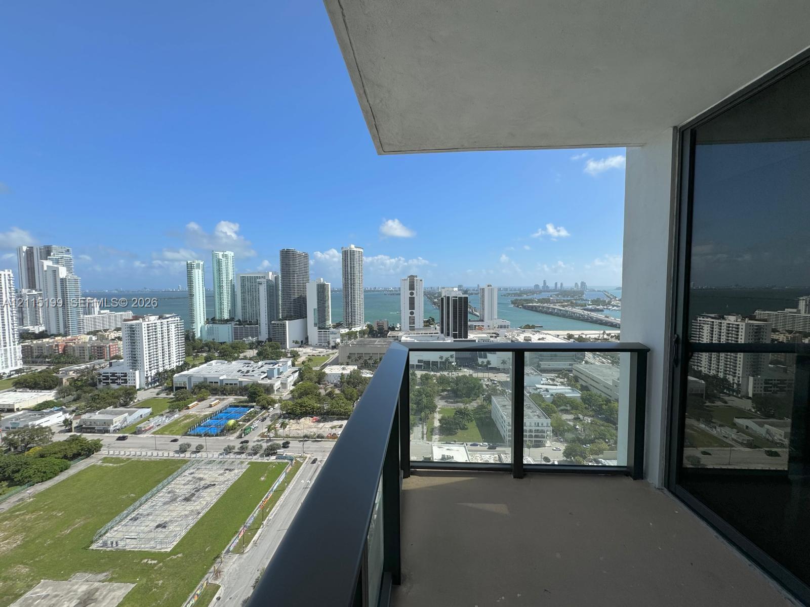 Private balcony featuring a dark metal railing with glass panels and concrete flooring, overlooking the cityscape and water