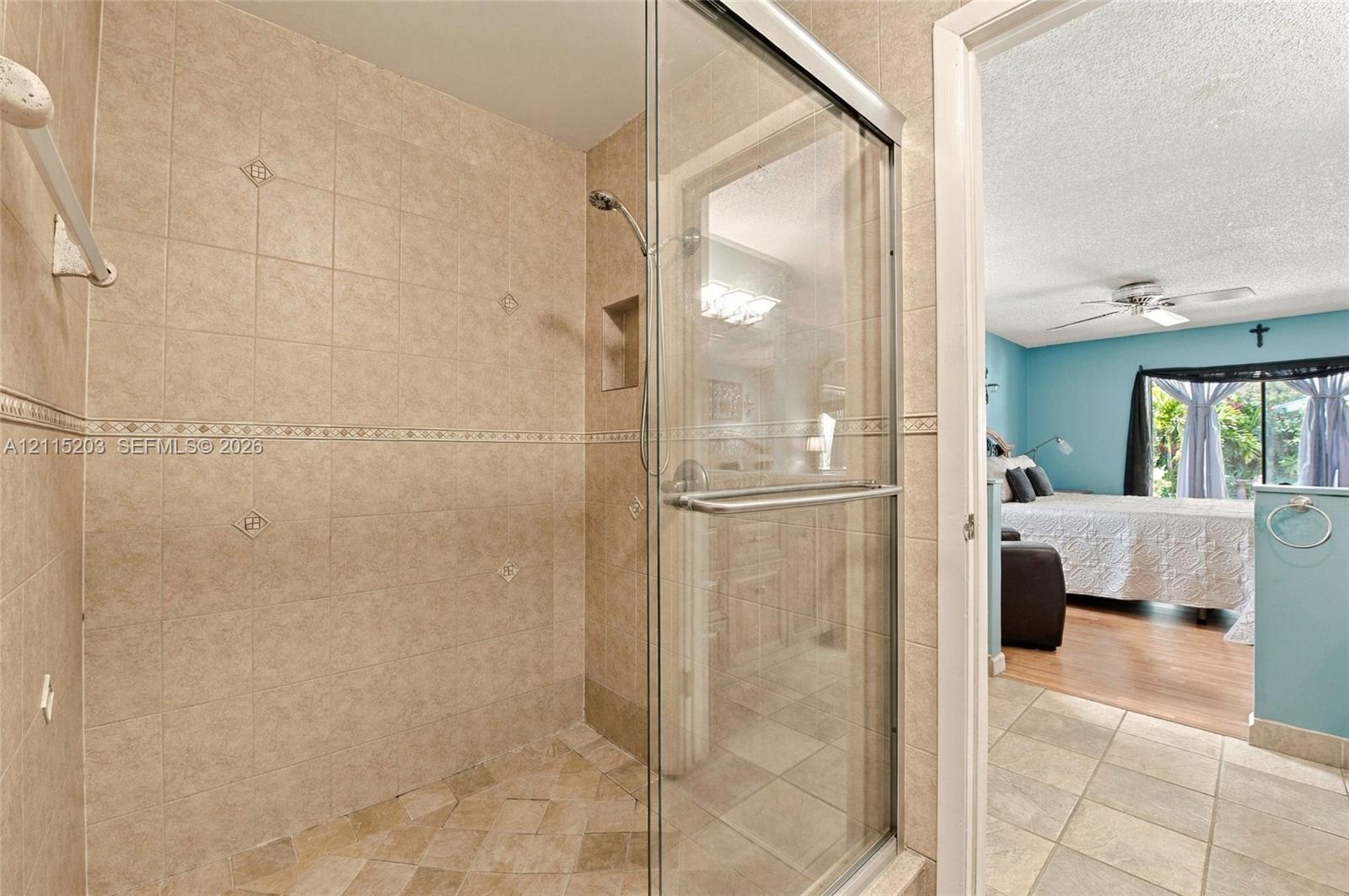 Walk-in shower featuring glass enclosure, ceramic tile surround with decorative accent inlay, recessed shelving, and a handheld shower fixture
