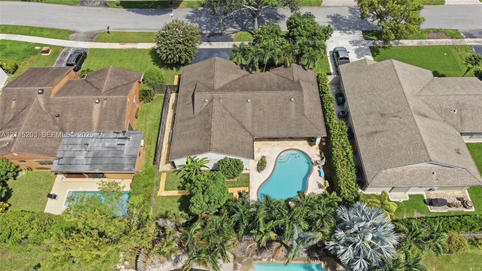 Aerial perspective featuring a 2019 shingled roof, a paved pool deck, and an in-ground swimming pool surrounded by mature landscaping Aerial perspective featuring a 2019 shingled roof, a paved pool deck, and an in-ground swimming pool surrounded by mature landscaping