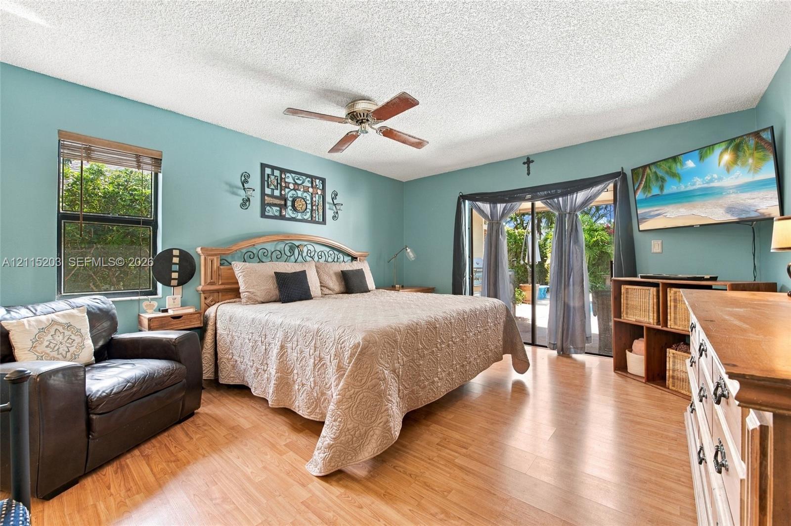Wood-finish flooring, ceiling fan with light fixture, large window with blinds, and sliding glass doors with exterior access