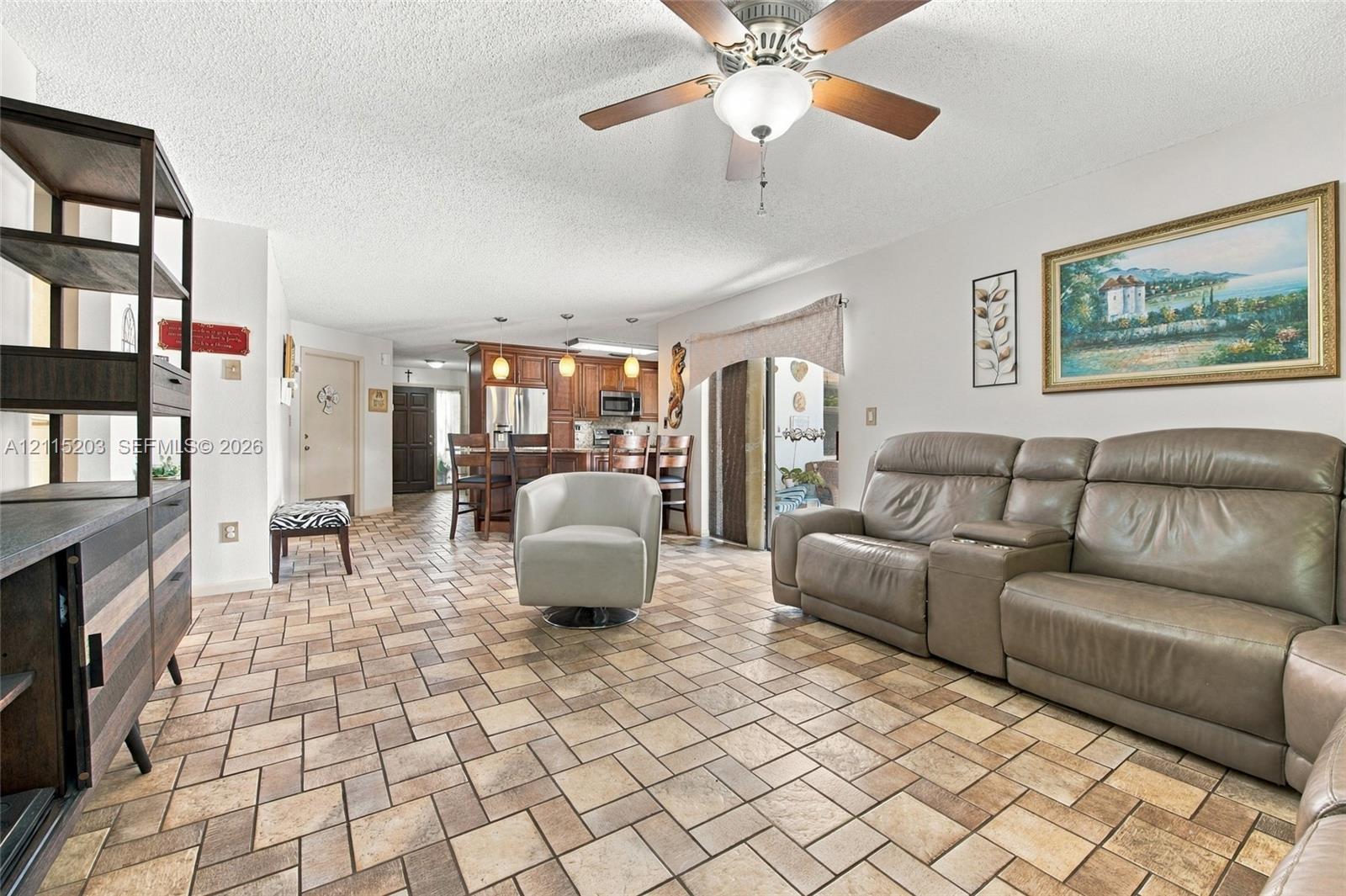 Open-concept interior featuring stone-tile flooring in a herringbone pattern, wood-finish cabinetry, built-in recessed lighting, and a ceiling fan with integrated lighting