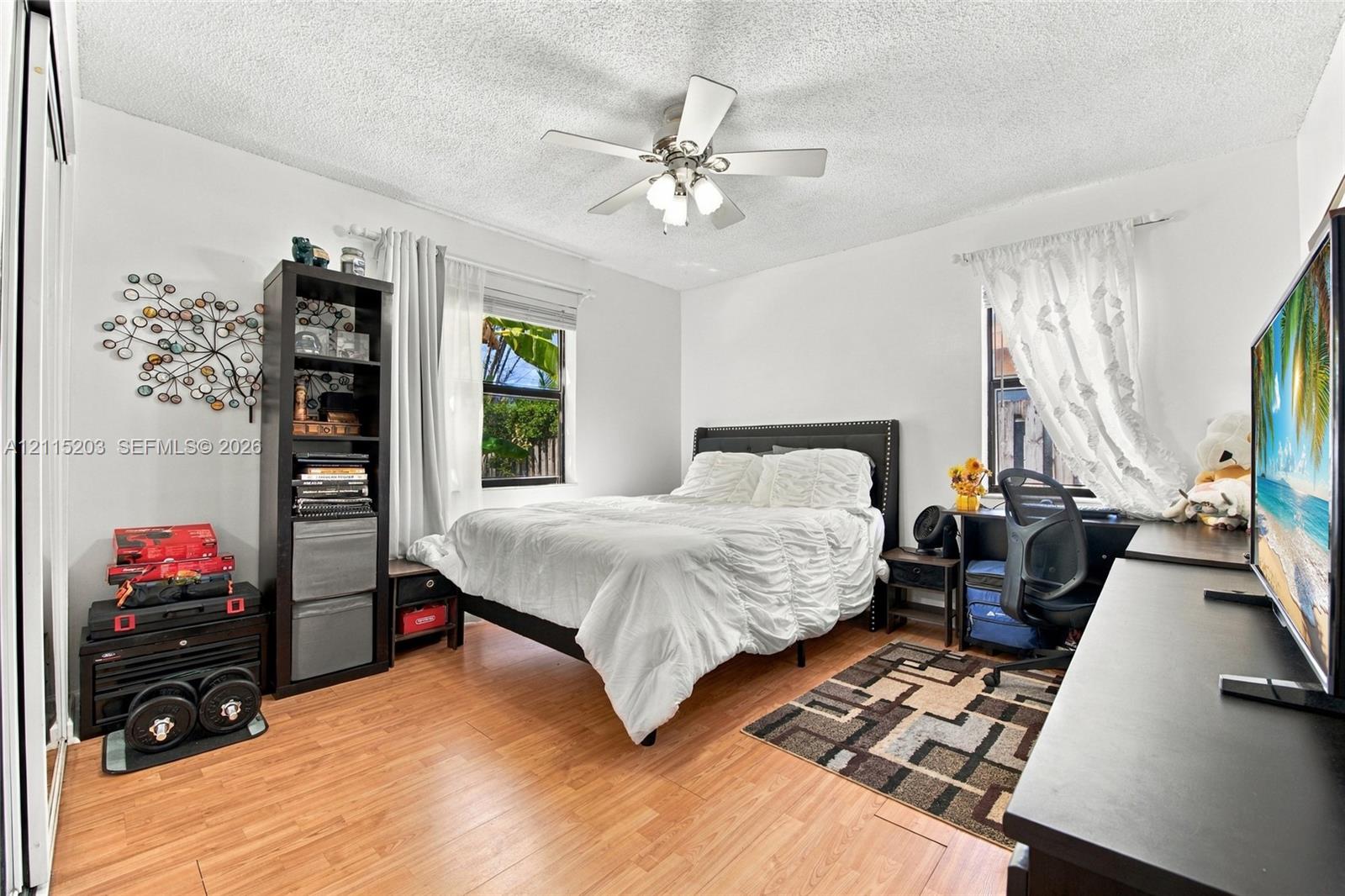 Bedroom featuring wood-finish flooring, dual windows, and a central ceiling fan with integrated light fixture