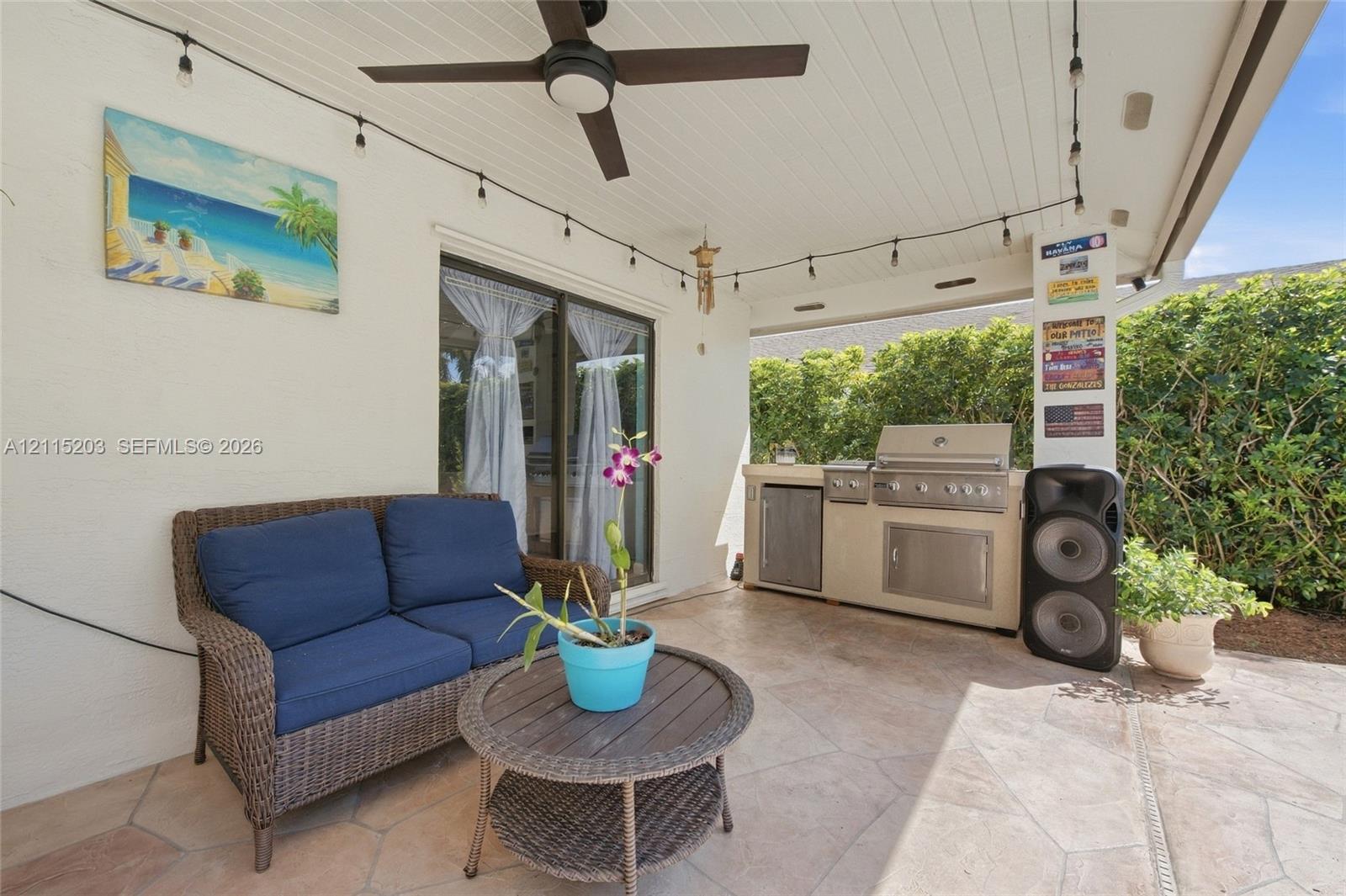 Covered outdoor patio featuring flagstone-style flooring, built-in stainless steel grill station with under-counter storage, ceiling fan, and beadboard ceiling Covered outdoor patio featuring flagstone-style flooring, built-in stainless steel grill station with under-counter storage, ceiling fan, and beadboard ceiling