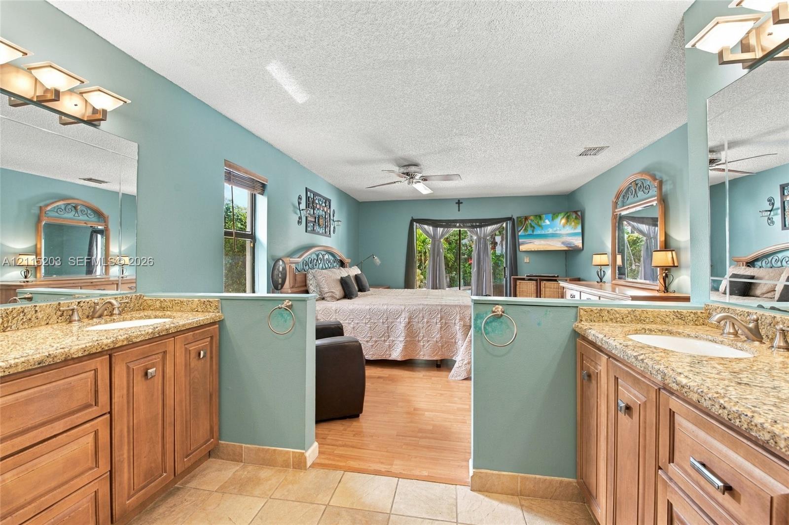 Dual-vanity bathroom featuring stone-finish countertops, warm-toned cabinetry, ceramic tile flooring, and integrated wall-mounted lighting