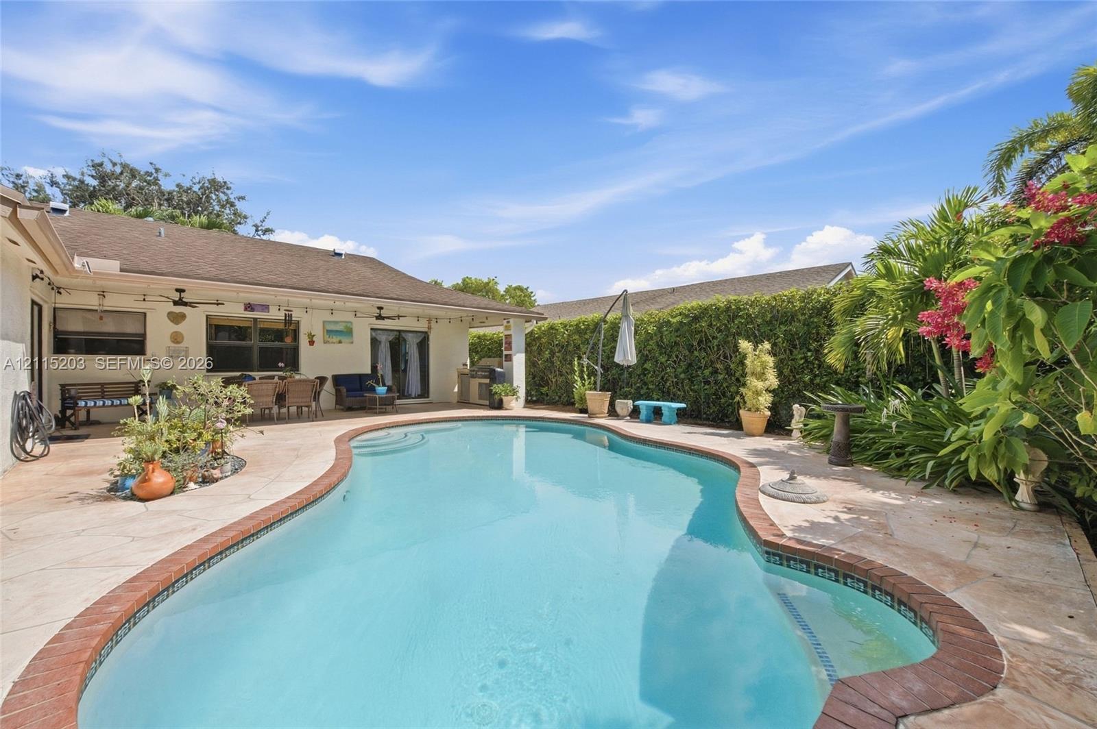 Custom-shaped swimming pool with brick coping, expansive stone-paver deck, and a covered lanai featuring ceiling fans and recessed lighting
