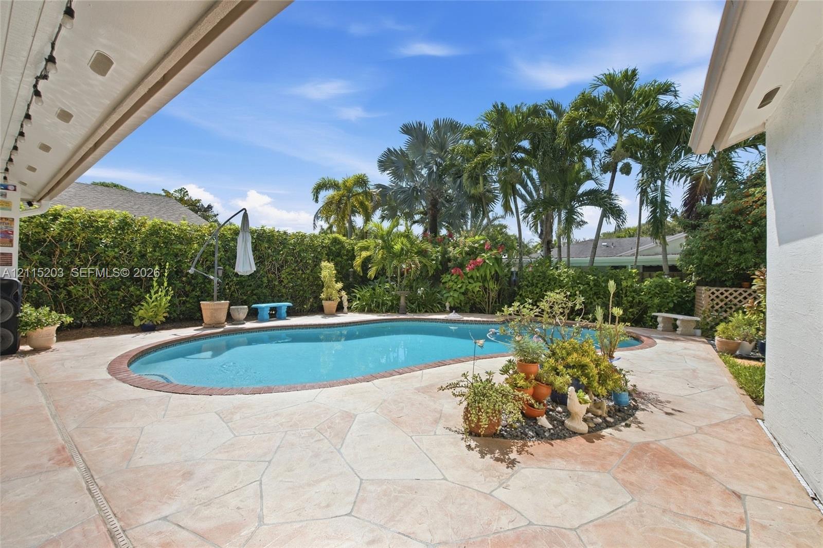 Outdoor pool area featuring flagstone decking, a brick pool coping, and lush privacy hedging