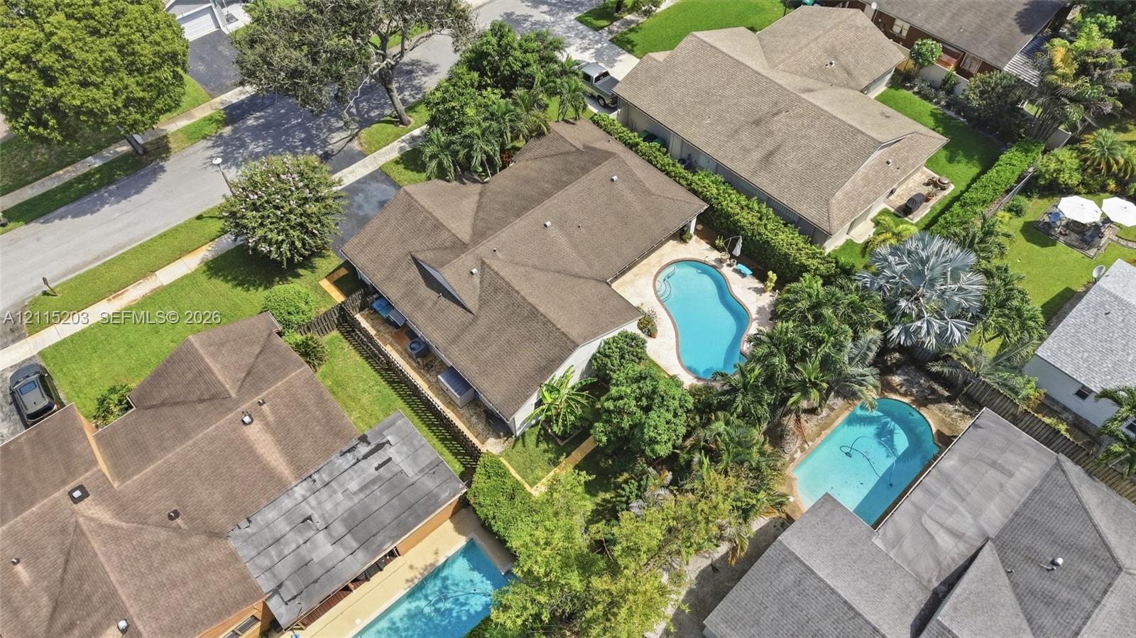 Aerial perspective featuring a multi-hipped roofline, an in-ground swimming pool, a concrete patio area, and mature perimeter landscaping Aerial perspective featuring a multi-hipped roofline, an in-ground swimming pool, a concrete patio area, and mature perimeter landscaping