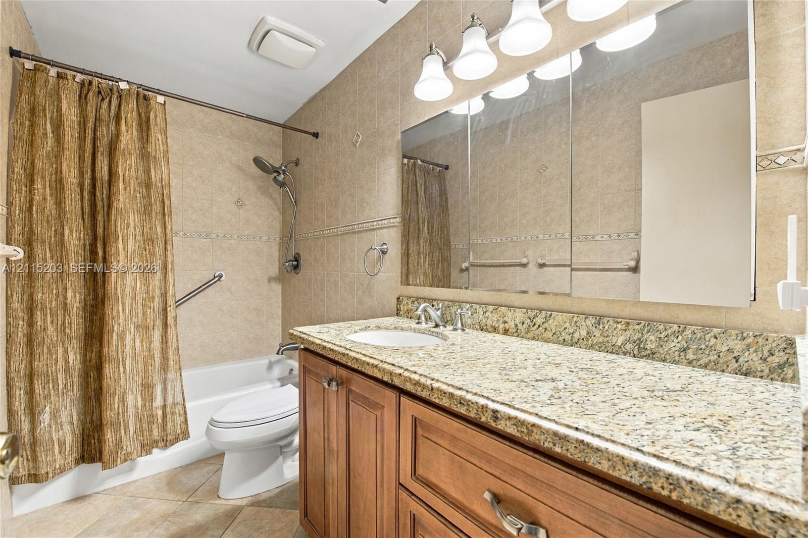 Bathroom featuring a vanity with stone-finish countertop, undermount sink, multi-light fixture, oversized vanity mirror, and tiled shower surround