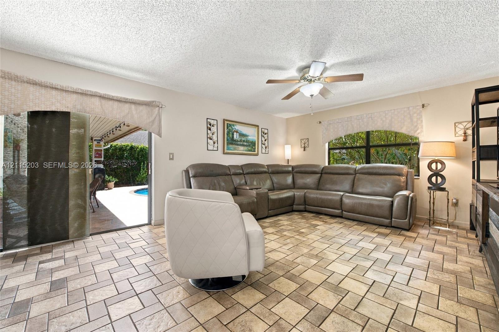 Living area featuring neutral-tone tile flooring, a ceiling-mounted light fixture with fan, and a large sliding glass door providing external access