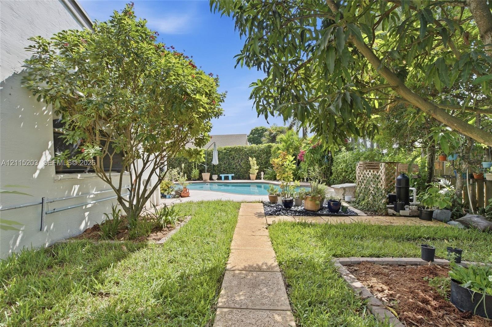Backyard featuring an in-ground swimming pool, concrete paver walkway, landscaped garden beds, and mature fruit trees Backyard featuring an in-ground swimming pool, concrete paver walkway, landscaped garden beds, and mature fruit trees