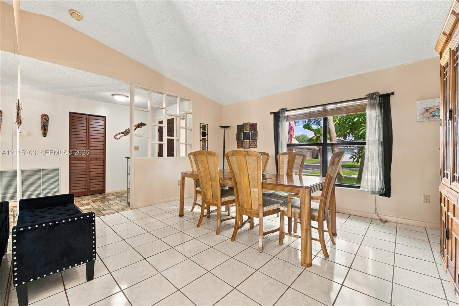 Volume ceilings, ceramic tile flooring, geometric lattice room divider, and large window with natural light