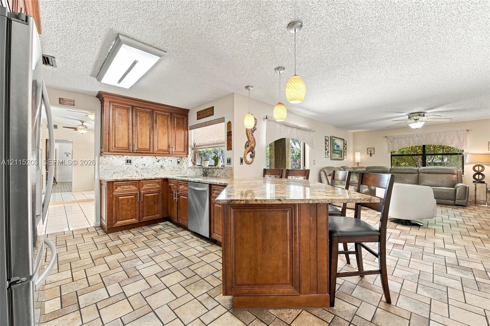 Kitchen featuring natural stone countertops, custom wood cabinetry, stainless steel dishwasher, stone-tile flooring, and glass pendant lighting